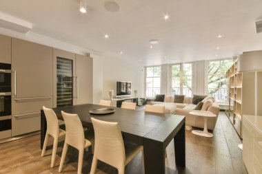 Ahşap döşemesi, beyaz sandalyeleri ve duvarında fırını olan modern bir dairede mutfak ve yemek odası.