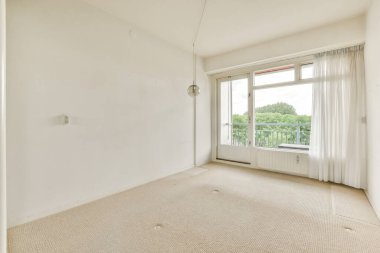 an empty living room with white walls and beige carpet, there is a window in the wall to the right
