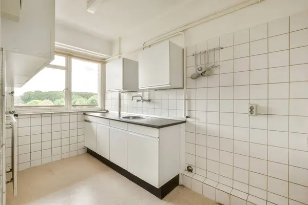 a kitchen with white tiles on the walls and counter space in front of the sink, window to the left