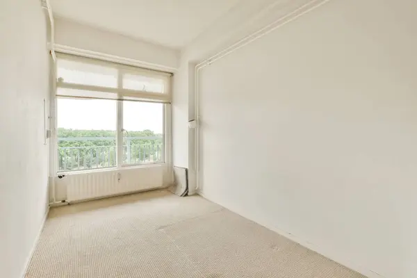 an empty room with white walls and beige carpeting, there is a window in the wall to the right