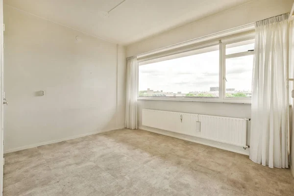 an empty room with white walls and beige carpet on the floor, there is a window that looks out to the city