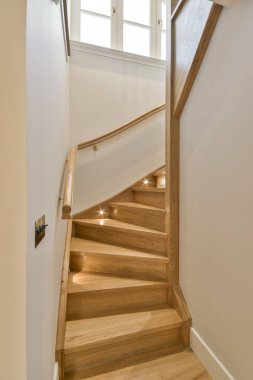 Beyaz duvarları ve hafif ahşap tırabzanları olan bir evin ikinci katına çıkan tahta bir merdiven.