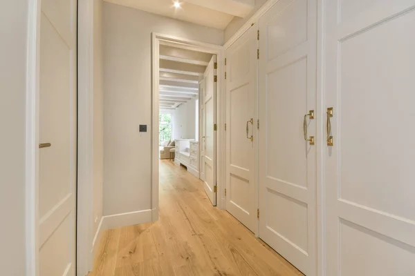 a long hallway with white doors and wood flooring on either side by side, leading to the living room