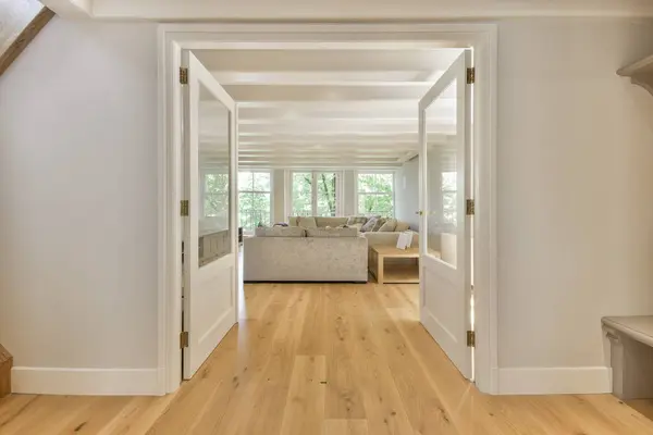a living room with hardwood flooring and white trim on the walls there is an open door leading to another room