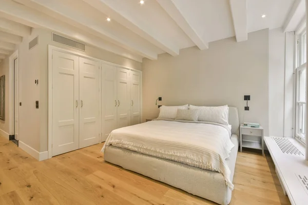 a bedroom with wood flooring and white walls, including a large bed in the center of the room is an air condition