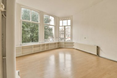 Boş bir oturma odası, ahşap döşeme ve evin önündeki sokağa bakan büyük pencereli.