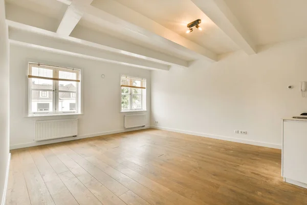 an empty living room with wood flooring and white walls, including two large windows in the room is very clean