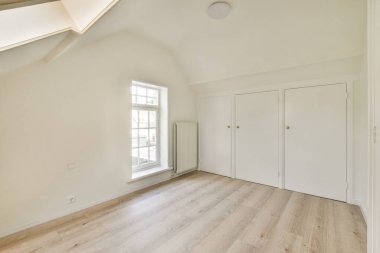 Beyaz duvarları ve ahşap döşemeleri olan boş bir oda, sağdaki duvarda bir pencere var.