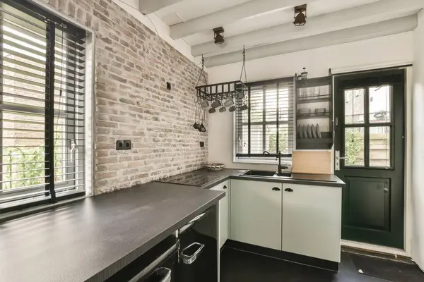 a kitchen with black counter tops and white brick wall in the background, there is an open window that looks out into the garden