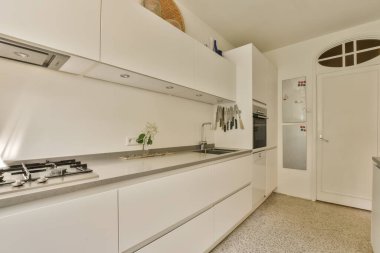 Fotoğrafın ortasında beyaz dolapları ve tezgahı olan modern bir mutfak ön kapıdan çekiliyor.