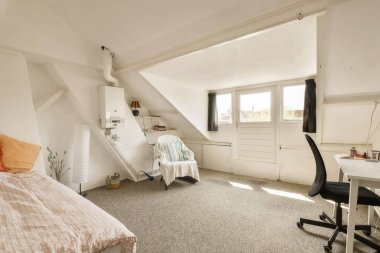 Yatağı, masası ve bilgisayarı olan bir yatak odası. Depoda kullanılan tavan arası tarzı bir odanın önünde.