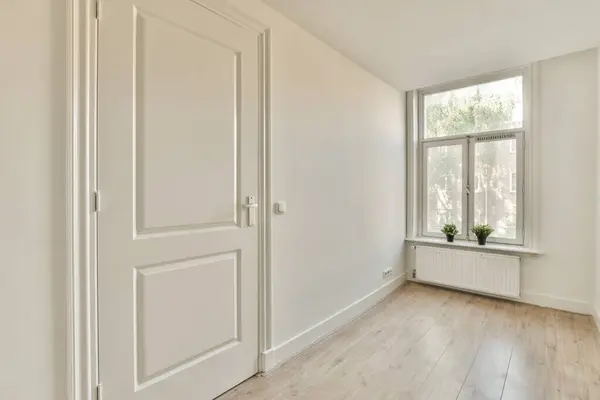 an empty room with white walls and wood flooring the door is open to reveal a window that looks out onto the street