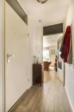 Ahşap döşemeli ve beyaz duvarlı bir koridor. Bir apartman dairesinde ya da konutta, ön kapıdan alınmış.