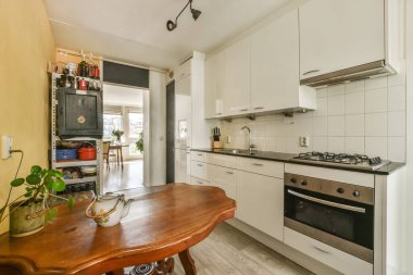 Odanın ortasında beyaz dolapları ve ahşap masası olan bir mutfak duvarda bir fırın var.