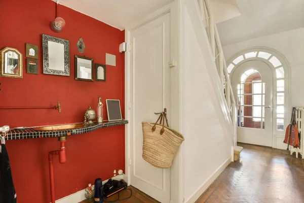 a hallway with red walls and white trim on the wall, there is a coat rack in front of the door
