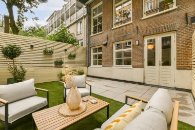 Kanepeler, masalar ve çiçeklerle bembeyaz boyanmış tuğla bir duvarın önünde.