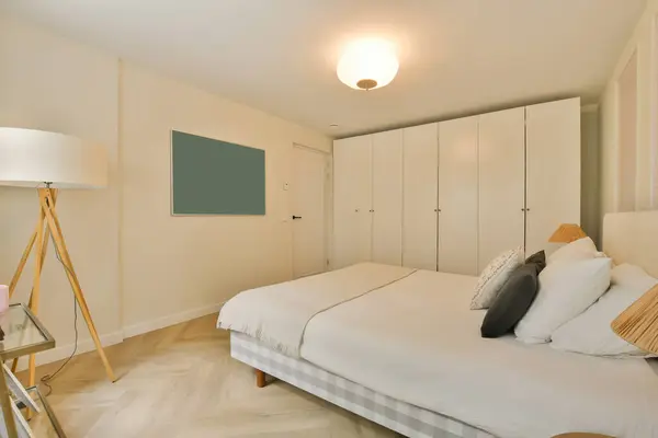 a bedroom with white walls and wood flooring, including a large bed in the room has a tv mounted on the wall