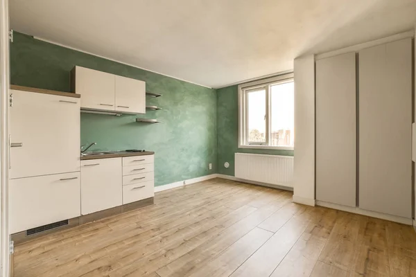 an empty kitchen with green walls and wood flooring in the middle of the room there is a white refrigerator