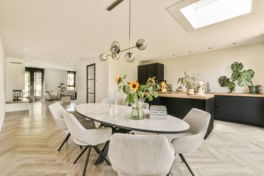 Odanın ortasında ahşap döşemeli ve siyah dolaplı bir yemek odası açık bir mutfak alanıdır.