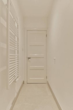 Her iki tarafında beyaz duvarlar ve döşemeler olan uzun bir koridor, ortada açık bir kapı var.