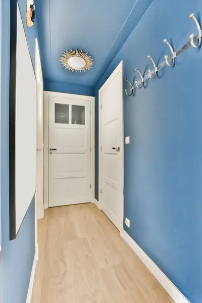 a hallway with blue walls and white trim on the ceiling, two doors are open to reveal an entryway