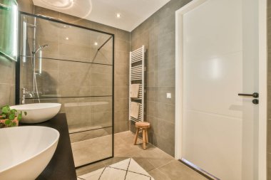 Duvarlarında gri fayanslar ve beyaz eşyalar olan modern bir banyo. Köşesinde de büyük bir ayna var.