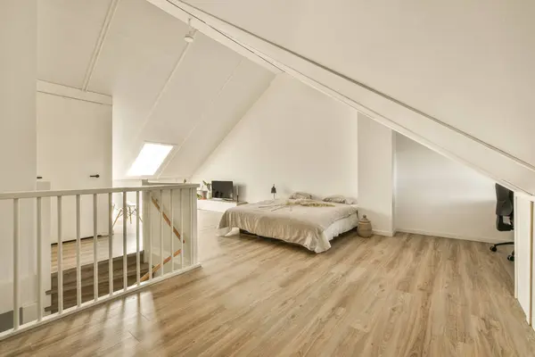 a bedroom with wood flooring and white walls in an attic - style home, showing the staircase leading up to the second floor