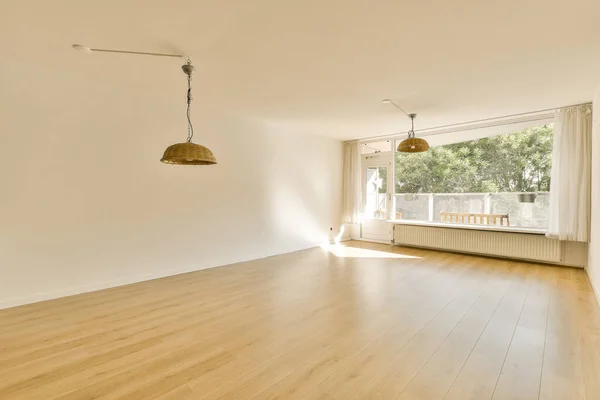 an empty living room with wood floor and ceiling fan in front of the window looking out onto the balcony area