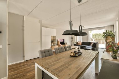 Açık bir alanda ahşap döşemeleri ve beyaz duvarları olan bir yemek odası. Gri sandalyelerle çevrili büyük ahşap bir masa da dahil.