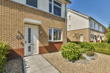 Açık mavi bir gökyüzünde, evin önünde bitkiler ve çalılarla dolu bir apartmanın önünde.