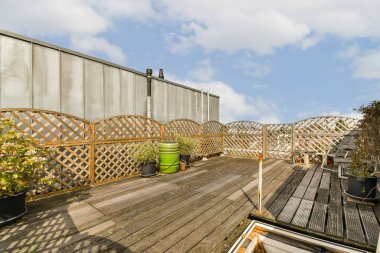 Arka planda bulutlu mavi bir gökyüzüne karşı, tencere ve bitkilerle dolu ahşap bir güverte.