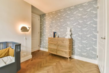 Duvar kağıdında gri ve beyaz kuşların olduğu bir bebek odası, ahşap kadife şifonyer ve masa değiştirme.