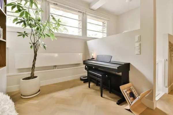 a living room with a piano and a plant in the corner on the right hand side of the photo is an open window