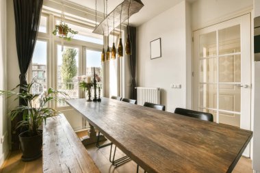 Ahşap masalı bir yemek odası ve balkon alanına açılan açık bir kapının önünde sandalyeler.