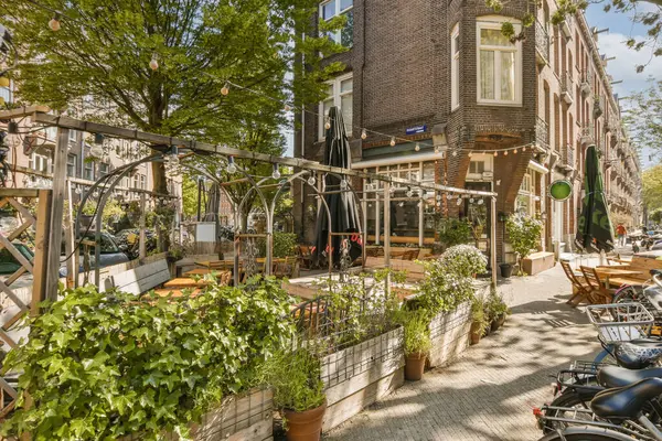 Önünde bisikletleri olan bir açık hava kafe ve sokağın kenarında ağaçlar var.