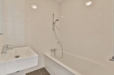 Lavabosu, aynası ve duş başlığı olan bir banyo. Duvara monte edilmiş. Küvetin yanında.