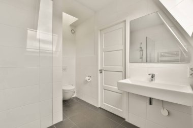 Siyah döşemeleri olan beyaz bir banyo ve açık bir kapı seni banyodaki tuvalete götürüyor.