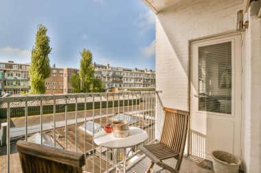 Dış masalı bir balkon ve sol tarafında sandalyeler var. Arka planda mavi bir gökyüzü var.