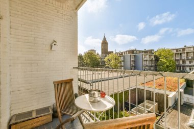 İki sandalyeli bir balkon ve pencerenin önünde şehir manzarasına bakan bir masa.
