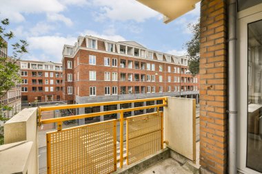 Turuncu çitli bir balkon ve güneşli bir günde arka planda bazı binalar.