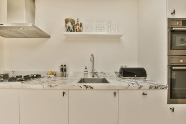 Mermer tezgahlı modern bir mutfak ve fotoğrafta beyaz dolaplar sağa doğru çekilirken, bulanık