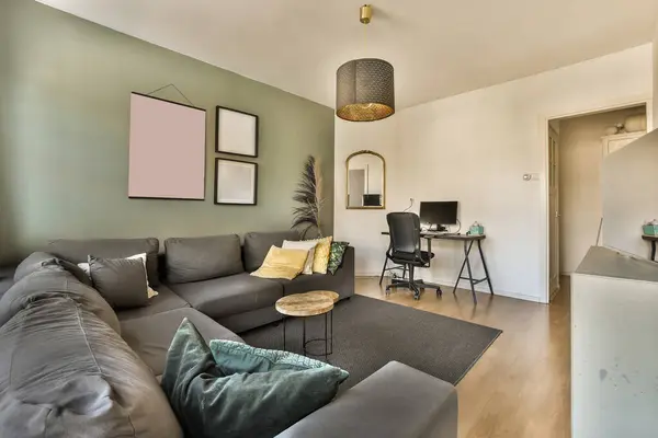 Gri kanepeleri ve duvarlarında yeşil aksanlı duvar kağıtları olan bir oturma odası, yerde açık bir mutfak ahşaptır.