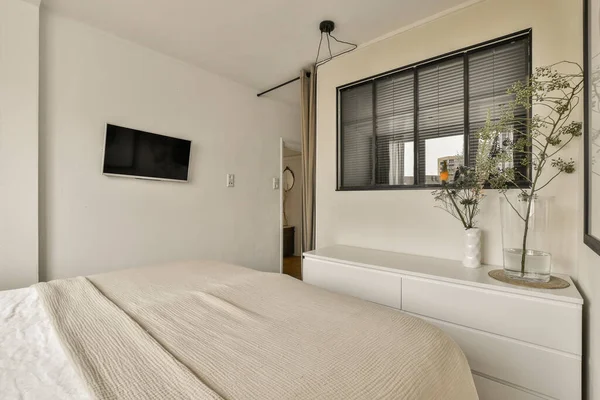 a bedroom with a bed, dresser and tv mounted on the wall in front of the bed is also white