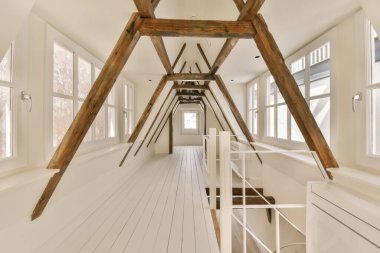 Tavanda beyaz duvarları ve tahta kirişleri olan bir oda. Çatı katına çıkan bir merdiven var.