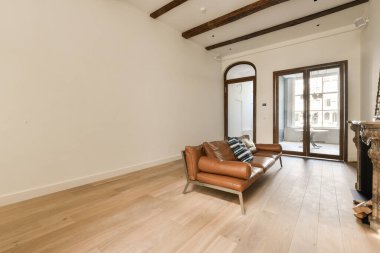 Tavanda ahşap döşeme ve açık kirişleri olan bir oturma odası şöminenin önünde kahverengi deri bir sandalye.