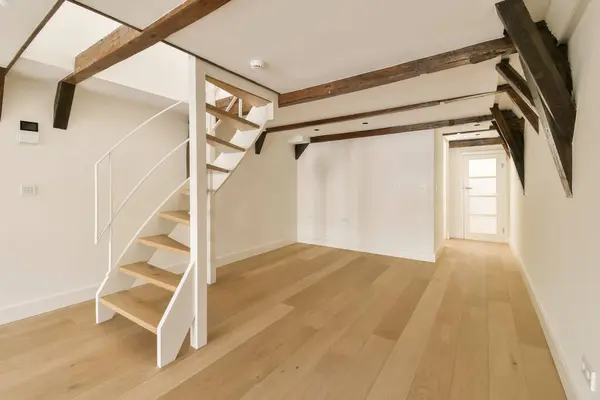 an empty room with wooden floors and white walls, there is a staircase leading up to the second floor in this home