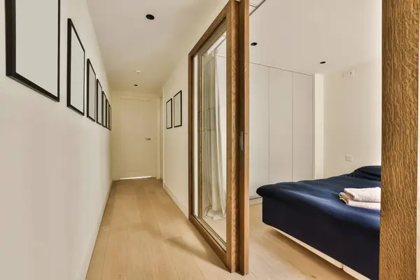 a bedroom with wood flooring and white walls on the wall, there is a large mirror in the room