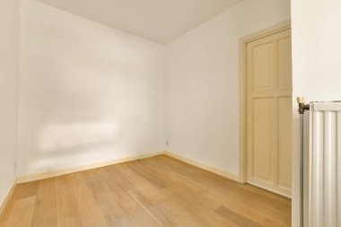 Ahşap zemini ve beyaz duvarları olan boş bir oda. Sağda da bir kapı var.