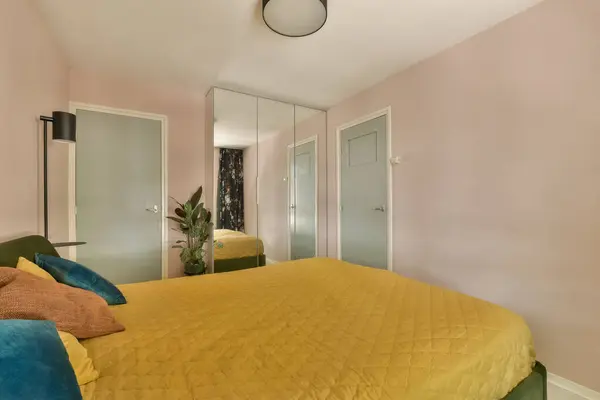 a bedroom with pink walls and yellow bedspremed comforter in the middle of the room is a mirror on the wall