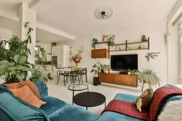 a living room with blue couches and green plants in the center of the room there is a tv on the wall
